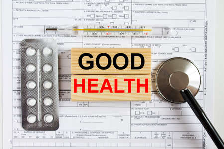 Text Good Health on jenga cubes with a stethoscope and pills are on medical documents. Medical concept photoの写真素材