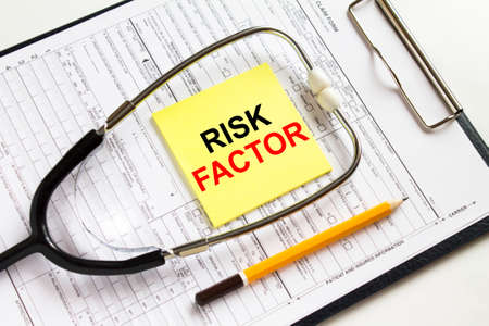 Text Risk Factor on a yellow sticker with a stethoscope lying on a folder with medical documents. Can be use as concept photoの写真素材