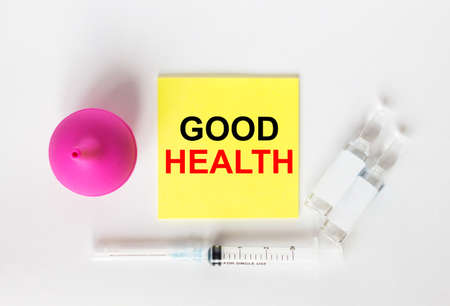 Yellow sticker with text Good Health on a white background with syringes, enema and ampoule. Medical concept photoの写真素材