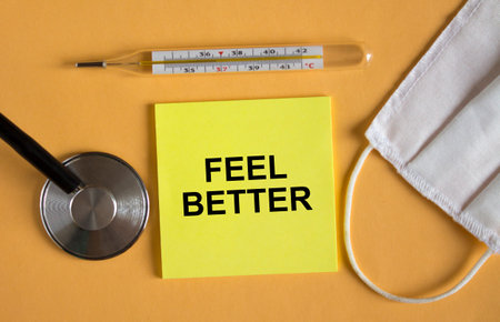 Sticker with text Feel Better lying on the orange background with mask and thermometer. Medical...