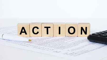 Action word concept written on wooden cubes blocks lying on a light table next to calculator and penの写真素材