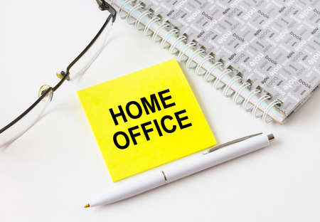 Text Home Office on a yellow sticker lying near notepad with eyeglasses and pen. Could be for business, financial and marketing conceptsの写真素材