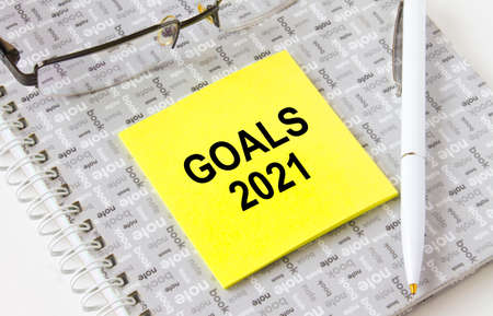 Text Goals 2021 on a yellow sticker lying on a notepad with eyeglasses and pen. Could be for business, financial and marketing conceptsの写真素材