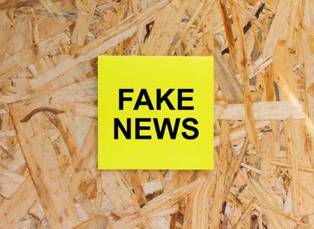Yellow Sticker with text Fake News on the wooden background. Concept photoの写真素材