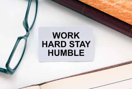 Text Work Hard Stay Humble on a business card lying next to notepad with eyeglasses and text documents. Business conceptの写真素材