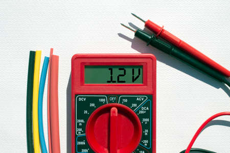 Multimeter with text on display 12 V and heat shrink insulation on white background. Construction and repairの写真素材