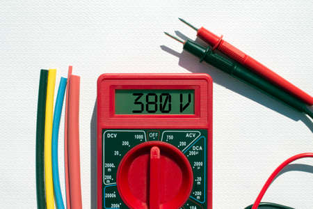 Multimeter with text on display 380 V and heat shrink insulation on white background. Construction and repairの写真素材