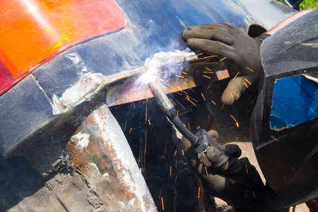 Welding industrial: worker in helmet repair detail in car serviceの写真素材