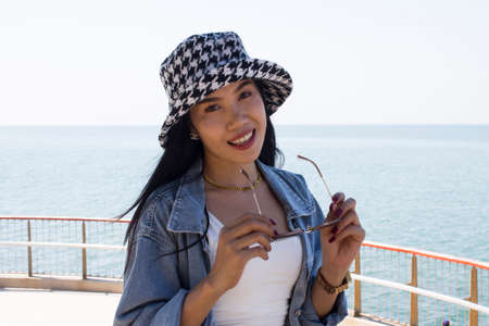 Beautiful asian woman holding black eyeglasses with hat on the sea. Can be use as concept photoの写真素材