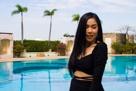 A smiling woman in black dress standing near swimming pool, leisure activities, holiday activities.の写真素材