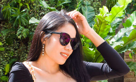 Young Asian Girl sitting in the garden and touches own hair. Can be used as concept photoの写真素材