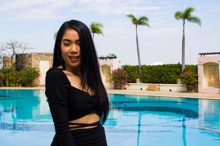 A smiling woman in black dress standing near swimming pool, leisure activities, holiday activities.の写真素材