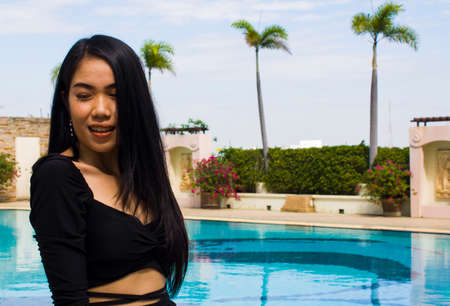 A smiling woman in black dress standing near swimming pool, leisure activities, holiday activities.の写真素材