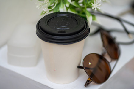 Coffee Cup and Eyeglasses on White Table in front of Green Plants Close Upの写真素材