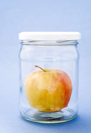 Apple of yellow-red color in the glass can under cover on blue backgroundの写真素材