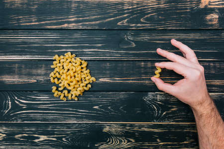 In male hands, pasta on black wooden background
