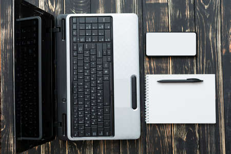Home workplace. Blank notebook, laptop, pen and mobile on a dark background niceの写真素材