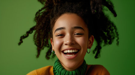 cheerful african american girl smiling and looking at camera isolated on greenの素材