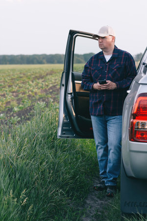 A man stands beside a car, engrossed in his cell phone.の写真素材