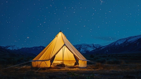 A tent illuminated by light stands out in the dark mountain landscape.の素材