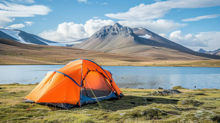 An orange tent is pitched on green grass next to a body of water in a beautiful summer landscape.の素材