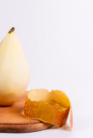 A close-up photograph of a yellow pear on a wooden cutting board with a piece of peeling beside it.の写真素材