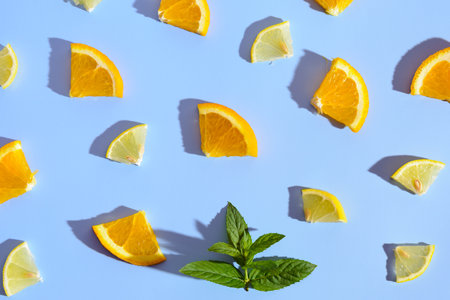 A flat lay image of orange and lemon slices arranged on a bright blue background, with a sprig of mint placed in the center.の写真素材