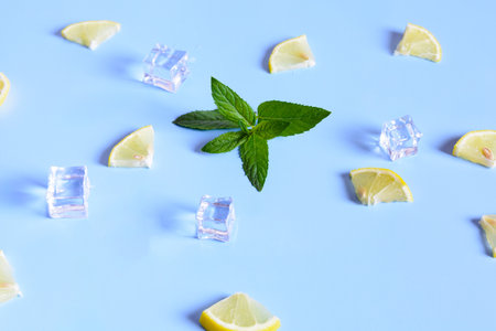 A close-up shot of fresh lemon slices, mint leaves, and ice cubes on a light blue background.の写真素材