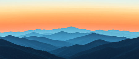 Layers of mountains unfold under a stunning dawn sky, where warm oranges blend with cool blues, highlighting the tranquil beauty of the landscape at sunrise.の素材