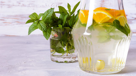 A glass pitcher filled with water, orange slices, mint leaves, and possibly other citrus fruits sits...