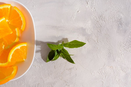 A close-up photo of a white plate with orange slices and a sprig of mint leaves on a white...