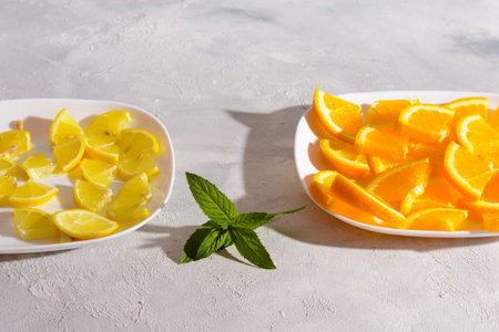 Sliced lemons and oranges on white plates with fresh mint on a light gray background.