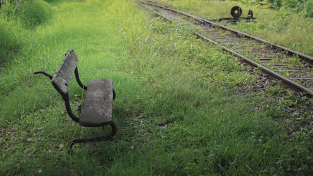 Old bench on a grassy field with train tracks. It could be used to illustrate a variety of concepts, such as nostalgia, travel, or simply a peaceful moment in nature.の写真素材