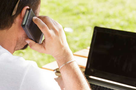 Man calling and typing with laptop in outdoors