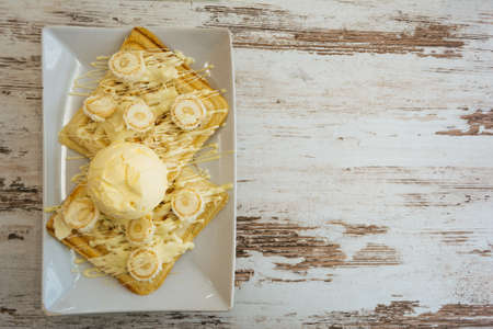 Belgian waffles with melted white chocolate, vanilla ice cream and coconut flakes on light wooden background.の写真素材