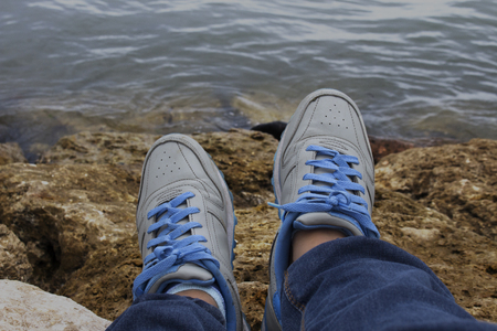 Top View of A Teenager Food Wear Jean and Blue Shoes Sitting on Brown Beach Stoneの写真素材