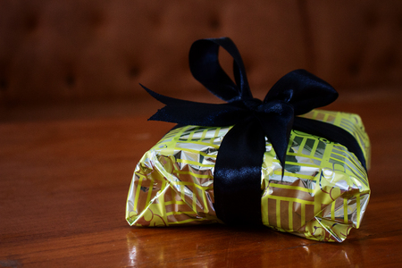 Gift Wrapped in Yellow and Silver Paper and Tied With Black Ribbon on Wood Deskの写真素材