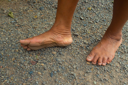 Close-up of a brown-skinned woman showing bare feet sole and heel on gravel, highlighting skin texture. Ideal for lifestyle, health, wellness, and natural beauty content.の写真素材