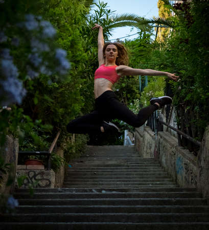Young fitness pretty girl jumps on the stairs on the street in the summer evening
