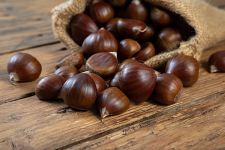 Fresh chestnuts in a burlap bag on a wooden background.の写真素材