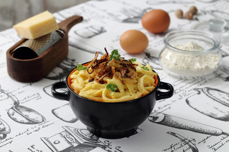 Tasty appetizing classic italian pasta carbonara in a black bowl with ingredients on the tableの写真素材