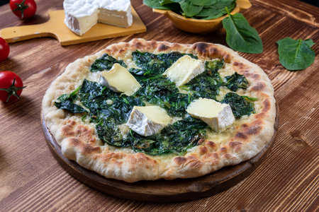 Pizza with spinach, cheese and cherry tomatoes on a wooden tableの写真素材