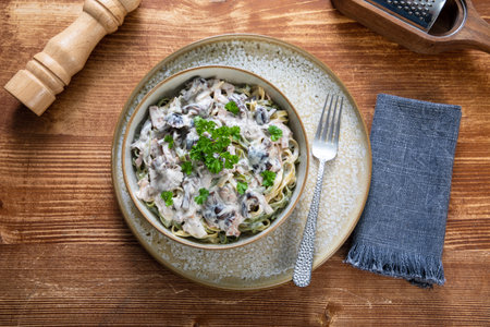 Pasta with mushrooms and cream sauce in a bowl on a wooden tableの写真素材
