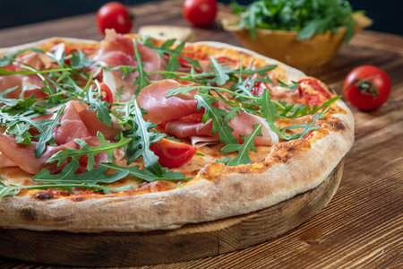 Pizza with prosciutto, arugula and cherry tomatoes on wooden tableの写真素材