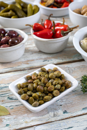 Pickled capers in bowls with pickles and olives on wooden background