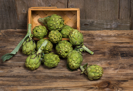 Fresh artichokes   in a basket is scattered on a rustic wooden table の写真素材