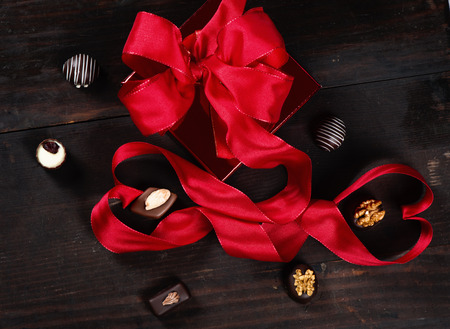 composition with box, chocolate candies and red ribbon shaped as hearts on a wooden old background, top viewの写真素材
