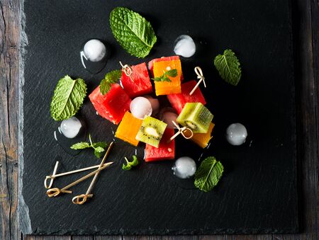 Top view of fruit salad with watermelon, oranges,  kiwi and ice on a black slate boardの写真素材