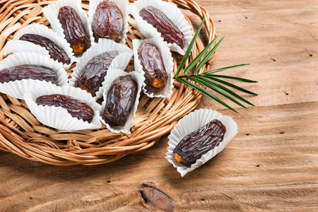 Date fruits medjool in individual packaging paper in a wicker tray on a wooden table.