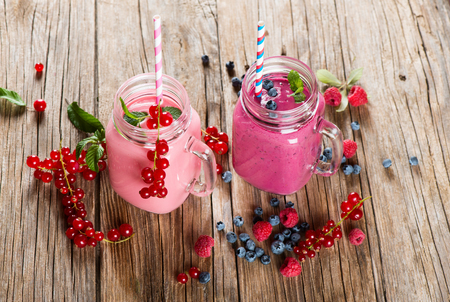 Smoothies of different berries with mint in mason jar mug with straw on a old wooden tableの写真素材